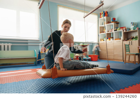 Balancing on the surface that is swinging. Preschool child with teacher during developmental activities in a playroom 139244260