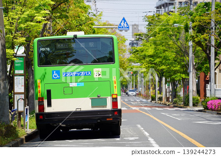 A Toei bus (rear view) departing from a bus stop on a street lined with zelkova trees. 139244273