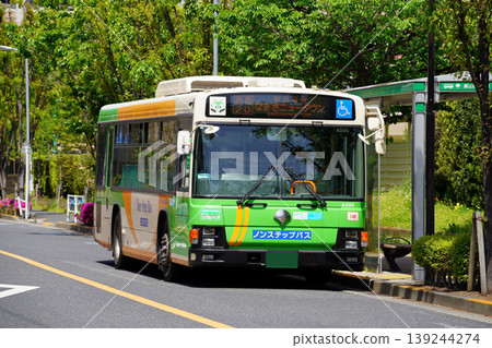 A Toei bus parked at a bus stop surrounded by greenery (close-up) 139244274