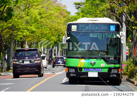 A close-up of a Toei bus (front view/Mitsubishi Aero Star) departing from a bus stop on a zelkova tree-lined street. A close-up of a Toei bus (front view/Mitsubishi Aero Star) departing from a bus stop on a zelkova tree-lined street. 139244279