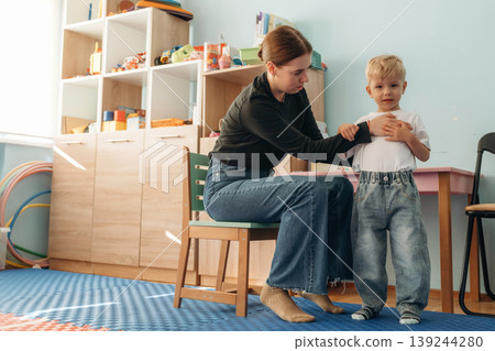 Woman is sitting and checking the boy. Preschool child with teacher during developmental activities in a playroom Woman is sitting and checking the boy. Preschool child with teacher during developmental activities in a playroom 139244280