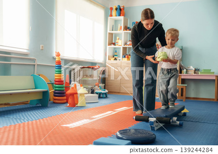 Balancing, walking. Preschool child with teacher during developmental activities in a playroom Balancing, walking. Preschool child with teacher during developmental activities in a playroom 139244284
