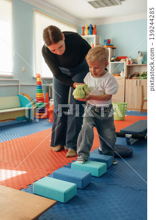 Balancing, walking. Preschool child with teacher during developmental activities in a playroom Balancing, walking. Preschool child with teacher during developmental activities in a playroom 139244285