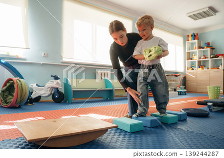 Balancing, walking. Preschool child with teacher during developmental activities in a playroom Balancing, walking. Preschool child with teacher during developmental activities in a playroom 139244287