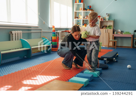 Doing balance training exercises. Preschool child with teacher during developmental activities in a playroom Doing balance training exercises. Preschool child with teacher during developmental activities in a playroom 139244291