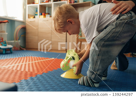Cute dragon toy head toy, using it. Preschool child with teacher during developmental activities in a playroom Cute dragon toy head toy, using it. Preschool child with teacher during developmental activities in a playroom 139244297