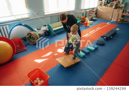 Path with cubes, balance training. Preschool child with teacher during developmental activities in a playroom Path with cubes, balance training. Preschool child with teacher during developmental activities in a playroom 139244299