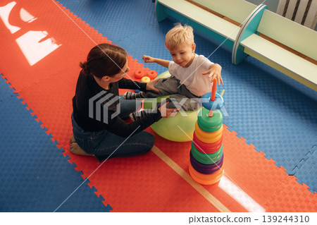 The balancing tricks on the ball. Preschool child with teacher during developmental activities in a playroom The balancing tricks on the ball. Preschool child with teacher during developmental activities in a playroom 139244310