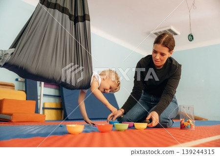 Putting the objects into bowls while hanging. Preschool child with teacher during developmental activities in a playroom Putting the objects into bowls while hanging. Preschool child with teacher during developmental activities in a playroom 139244315