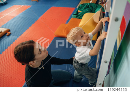 Climbing the ladder that is on the wall. Preschool child with teacher during developmental activities in a playroom 139244333