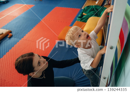 Climbing the ladder that is on the wall. Preschool child with teacher during developmental activities in a playroom 139244335