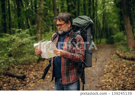 Paper map is in hands. Hiking experience, senior man is in the forest at daytime 139245139