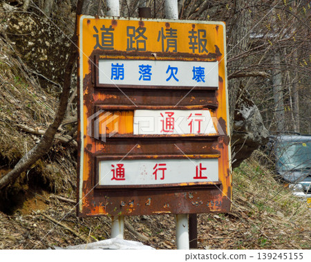 A rusty road information sign indicating a road closure due to collapse and damage. A rusty road information sign indicating a road closure due to collapse and damage. 139245155