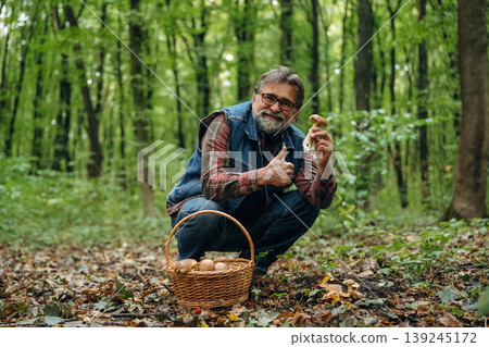 Positive facial expression, smiling. Mushroom picking. Man is in the forest at daytime Positive facial expression, smiling. Mushroom picking. Man is in the forest at daytime 139245172