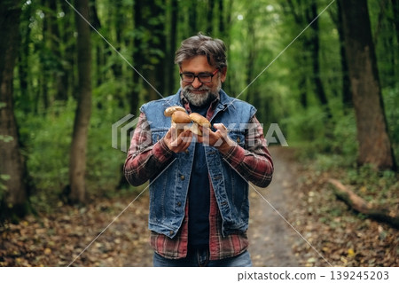 Raw food is in hands. Mushroom picking. Man is in the forest at daytime Raw food is in hands. Mushroom picking. Man is in the forest at daytime 139245203
