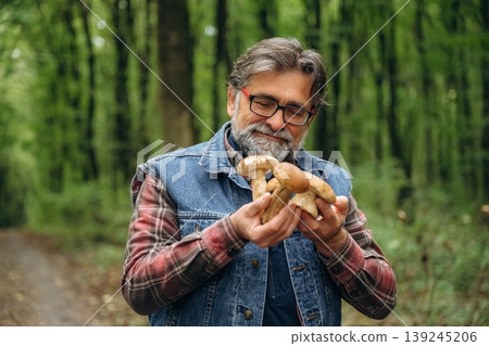 Raw food is in hands. Mushroom picking. Man is in the forest at daytime Raw food is in hands. Mushroom picking. Man is in the forest at daytime 139245206