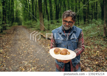 In the hat, holding in hands. Mushroom picking. Man is in the forest at daytime In the hat, holding in hands. Mushroom picking. Man is in the forest at daytime 139245214