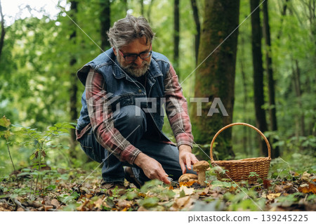 In jacket, with basket. Mushroom picking. Man is in the forest at daytime In jacket, with basket. Mushroom picking. Man is in the forest at daytime 139245225