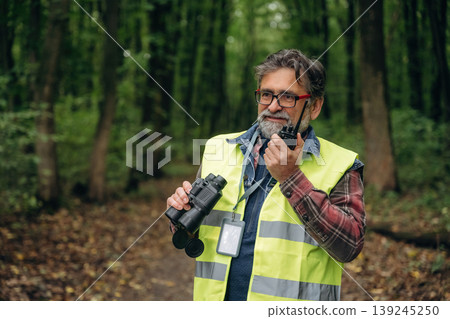 Talking by walkie talkie. Senior forest ecologist is working in the woods. In the uniform Talking by walkie talkie. Senior forest ecologist is working in the woods. In the uniform 139245250