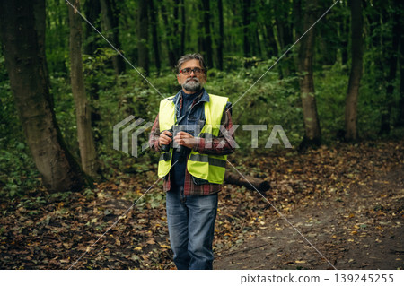 Professional binoculars in hands. Senior forest ecologist is working in the woods. In the uniform 139245255