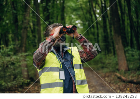 Professional binoculars in hands. Senior forest ecologist is working in the woods. In the uniform Professional binoculars in hands. Senior forest ecologist is working in the woods. In the uniform 139245258