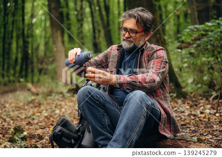 Pouring water from thermos. Hiking experience, senior man is in the forest at daytime 139245279
