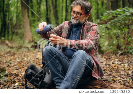Pouring water from thermos. Hiking experience, senior man is in the forest at daytime 139245280