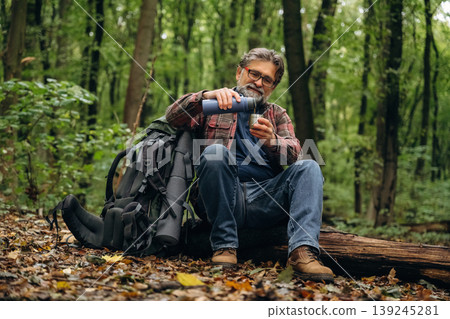 Pouring water from thermos. Hiking experience, senior man is in the forest at daytime 139245281