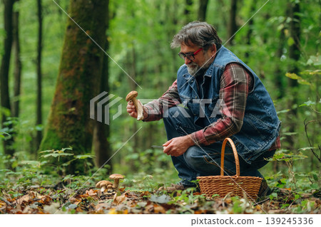 Focused, sitting and checking if it's safe one. Mushroom picking. Man is in the forest at daytime Focused, sitting and checking if it's safe one. Mushroom picking. Man is in the forest at daytime 139245336