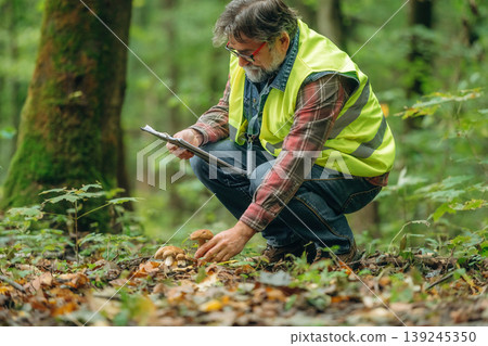 Gathering information, reading from notepad. Senior forest ecologist is working in the woods. In the uniform Gathering information, reading from notepad. Senior forest ecologist is working in the woods. In the uniform 139245350