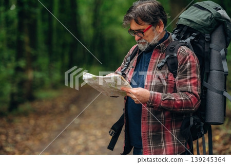Looking for the way, using map. Hiking experience, senior man is in the forest at daytime Looking for the way, using map. Hiking experience, senior man is in the forest at daytime 139245364