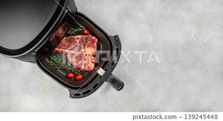 Raw porterhouse steak in open air fryer basket with herbs and cherry tomatoes on light concrete background, top view. copy space Raw porterhouse steak in open air fryer basket with herbs and cherry tomatoes on light concrete background, top view. copy space 139245448