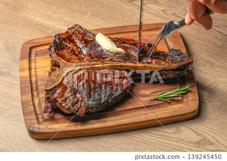 Cutting juicy grilled tomahawk steak with melting butter on wooden board close up food experience Cutting juicy grilled tomahawk steak with melting butter on wooden board close up food experience 139245450
