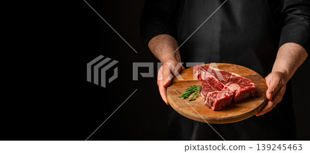 Man holding wooden board with raw t-bone steak on dark background. copy space 139245463