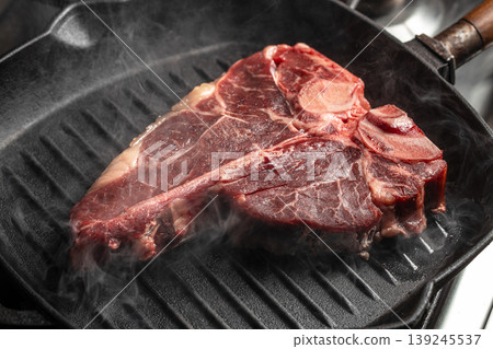 Raw t-bone steak cooking on grill pan with smoke, close up 139245537