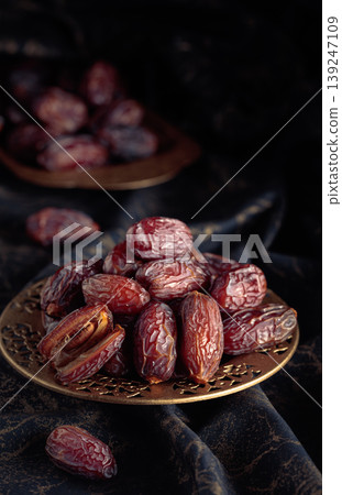 Dates fruits in a golden bowl on black fabric with gold ornamentation. Dates fruits in a golden bowl on black fabric with gold ornamentation. 139247109