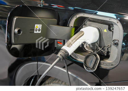 Electric vehicle charging port close-up with plugged charger connector on modern black EV car 139247657