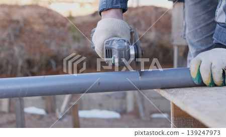 Worker Hands Cutting Metal Pipe With Angle Grinder On Outdoor Workbench Gloved Hands Hold Pipe Steady, Focused Closeup, Construction Background, Concrete Pavers And Fencing, Dust And Metal Worker Hands Cutting Metal Pipe With Angle Grinder On Outdoor Workbench Gloved Hands Hold Pipe Steady, Focused Closeup, Construction Background, Concrete Pavers And Fencing, Dust And Metal 139247973