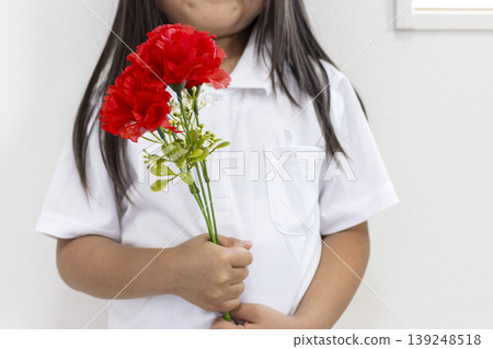 一個5歲日本女孩(沒有臉)拿著一朵人造紅色康乃馨。 一個5歲日本女孩(沒有臉)拿著一朵人造紅色康乃馨。 139248518