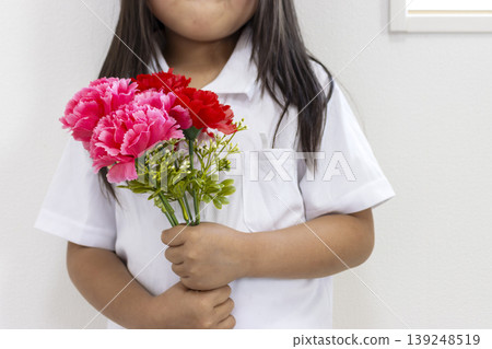 一個5歲日本女孩(沒有臉)拿著一朵人造紅色康乃馨。 一個5歲日本女孩(沒有臉)拿著一朵人造紅色康乃馨。 139248519