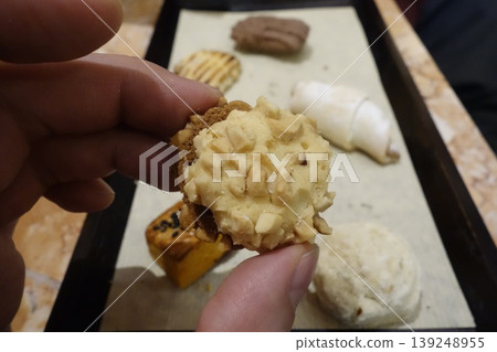 Hand Holding Nuts-Topped Pastry with Assorted Baked Goods 139248955