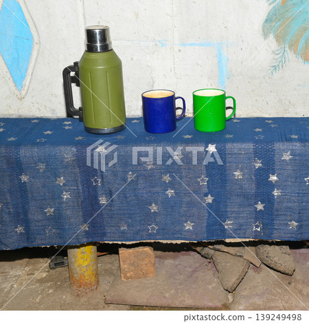 green thermos and two mugs stand on a long bench covered with blue fabric with stars green thermos and two mugs stand on a long bench covered with blue fabric with stars 139249498
