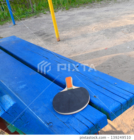 table tennis racket lies on a blue wooden bench outdoors table tennis racket lies on a blue wooden bench outdoors 139249510