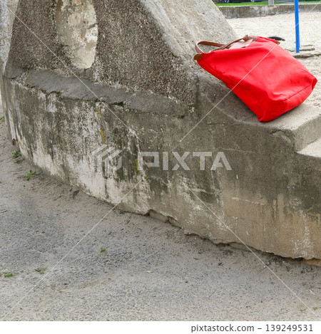 red women bag lies on a concrete ledge of a staircase on the street against the background of sand red women bag lies on a concrete ledge of a staircase on the street against the background of sand 139249531