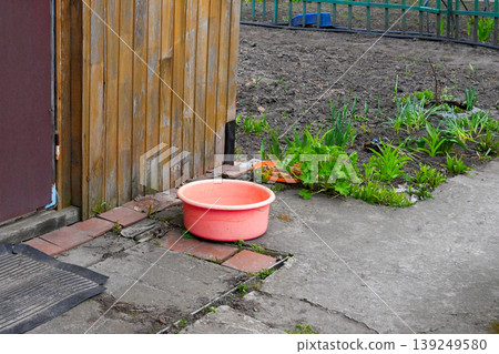 pink plastic basin stands on a concrete path in the garden against a wooden shed and beds pink plastic basin stands on a concrete path in the garden against a wooden shed and beds 139249580