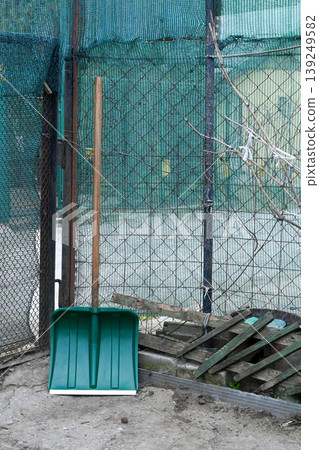 green plastic snow shovel on a wooden handle stands by a fence in the garden in spring 139249582