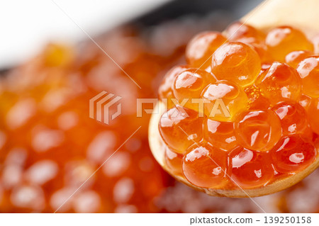 A vibrant orange photo of soy sauce-marinated salmon roe served on a spoon. A vibrant orange photo of soy sauce-marinated salmon roe served on a spoon. 139250158