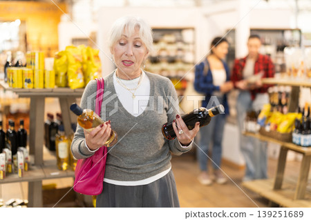 Elderly woman buyer chooses bottle of wine in store Elderly woman buyer chooses bottle of wine in store 139251689