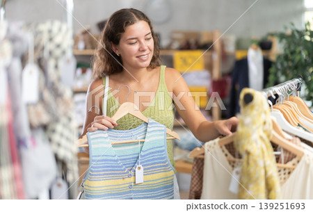 Positive young woman choosing something for summer in clothing store Positive young woman choosing something for summer in clothing store 139251693