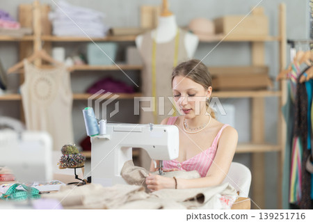 Young seamstress sews a dress on a machine Young seamstress sews a dress on a machine 139251716
